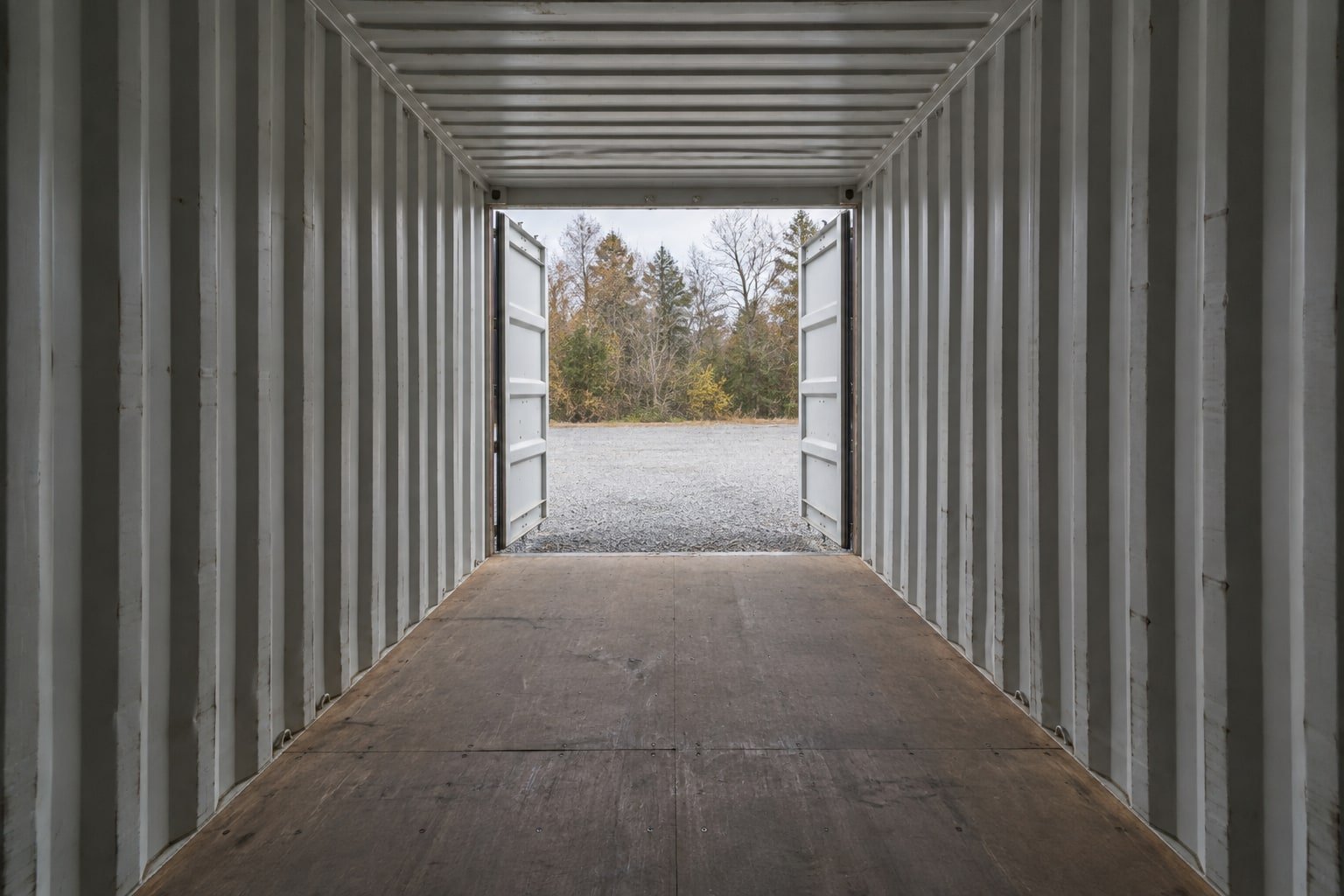 View from inside an empty storage container toward its open doors and a gravel yard.